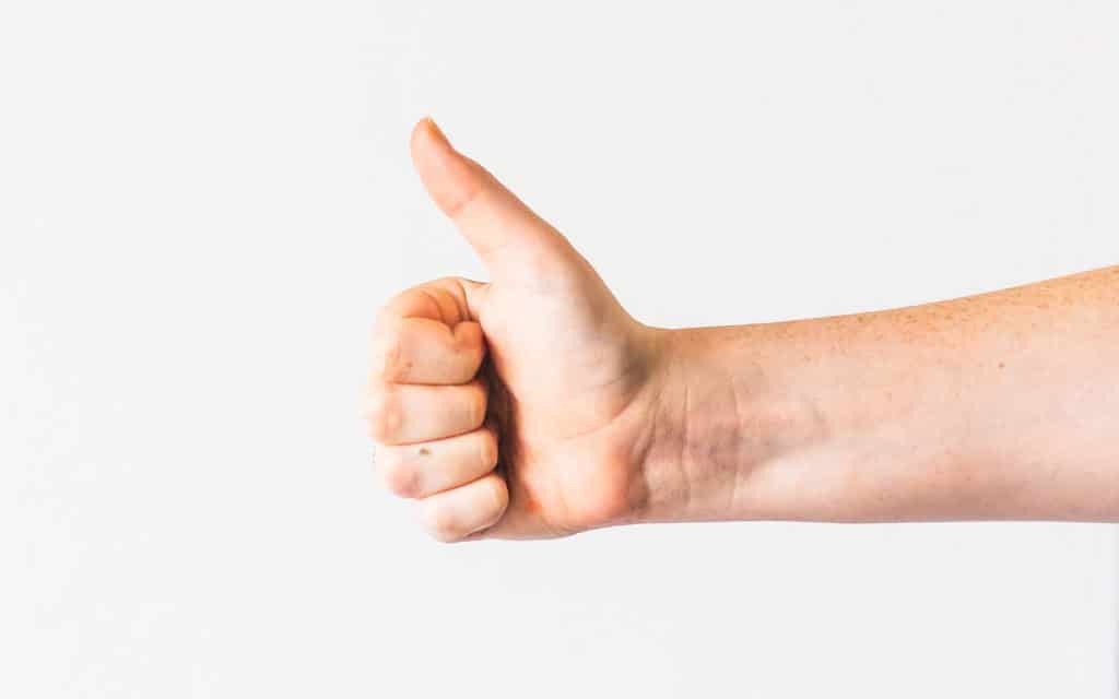 A hand against a blank wall giving the "Thumbs up" sign for "good".