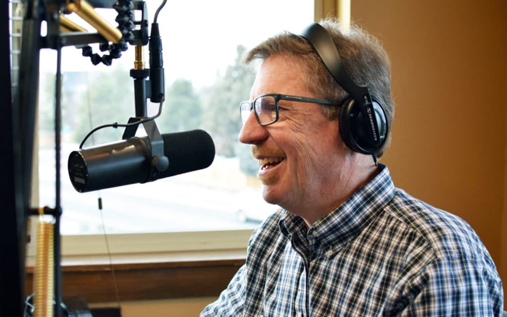 Side view of Fred. Fred Johnson has headphones on while he speaks into a microphone and smiles.