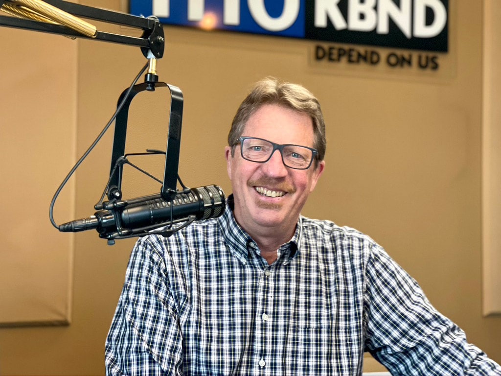 Image of Fred Johnson in a plaid shirt smiling. A microphone to record his podcast is next to him.